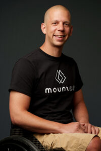 Porträt Stephan Gmür. Er sitzt im Rollstuhl und trägt ein schwarzes T-Shirt mit der Aufschrift MountOn.